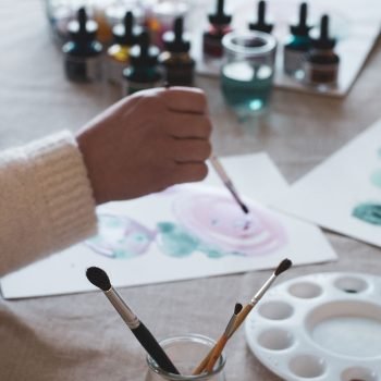 main qui tient un pinceau et qui peint une aquarelle